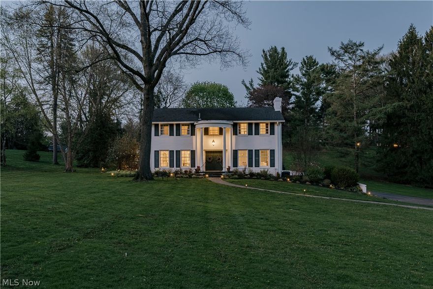 Set on a large lot in the sought-after Hills & Dales neighborhood of Canton, this Colonial Revival offers timeless architecture and refined living. A winding walkway leads to double doors framed by a curved portico with full-height columns, creating a striking first impression. The center-hall layout includes a substantial first-floor primary suite and laundry room addition that enhances space and function. The foyer features hardwood floors that extend through much of the main level. From here, the home opens to a formal dining room on one side and a spacious living room on the other. The living room is filled with natural light from large windows and features elegant wainscoting and a fireplace with dentil molding, pilasters, and a marble surround. The formal dining room includes two corner built-ins with arched glass doors and decorative detailing. The dining room connects to a well-appointed kitchen with a full appliance package, ample cabinetry, tile backsplash, granite countertops, and a center island. A large flex space off the kitchen is used as an informal dining area or playroom and opens to an enclosed porch. The family room features built-in bookshelves flanking a fireplace and includes a wet bar. Café doors lead to a hallway with a coffered ceiling that connects to the primary suite. The primary suite includes a vaulted bedroom with skylight, an ensuite bath with dual vanities, soaking tub, and step-in shower, plus a large walk-in closet with built-ins and a private laundry room. An elevator connects to the lower level but is currently non-functional. Upstairs, four bedrooms offer comfortable layouts. One includes a private ensuite bath. Two share a Jack-and-Jill bathroom. The fourth is near a full hall bath, ideal for guests. The full basement includes a recreation room, potting room, three garage bays, and ample storage. The backyard features a stone patio and mature garden beds. A recent inspection report is available in the supplements.