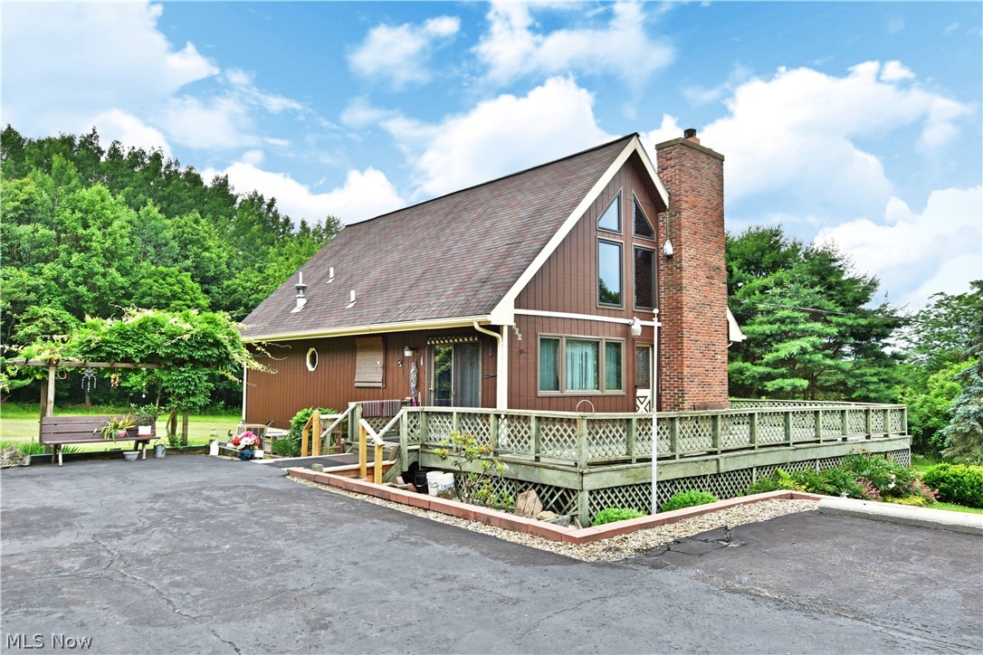 Get lost in the scenic countryside with this gorgeous Kinsman home! Offering up a unique, A-frame styling with a massive, wrapping deck; you’ll find eye catching views both inside and out! The expansive property places the residence far off the road with a large turnaround set before a substantial outbuilding with two garage entrances. The park-like landscaping entails multiple trellis and a charming gazebo that join planting boxes and tiered walkways. A towering brick chimney runs up the side of the home as you make your way inside. Through the front door, the open layout and tall ceiling blow you away with lavish woodwork from floor to ceiling as the dark stains are enriched by the natural light found pouring from the front windows. A picketed catwalk looks down on the great room below, taking in the robust kitchen, casual dining areas and handsome stone fireplace. Oriental styling garnishes the third upstairs bedroom and continues below as two other inviting rooms line the main hall