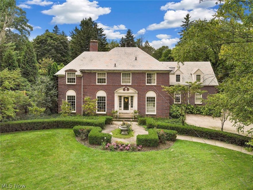 Spectacular brick Georgian Colonial on stately 1.37 acre lot. Stunning original details include slate roof, large crown moldings in formal rooms, original iron doors & accents, matching chandeliers and brass door knobs. Sealed entry leads to the large foyer. Formal living rm to the left with fireplace & door to 3-season rm. To the right is the library/study. The formal dining room with massive built-in cabinetry at the rear is between the sun room with newer windows and LVT flooring and the kitchen. The breakfast nook has bowed windows looking out to the rear yard and leaded window into the dining room. The 3-car attached garage entrance is nicely situated by the kitchen, half bath, and staircase to the basement. Oak flooring  throughout. The open staircase with curved volute cascades and is open at the 2nd floor foyer with built-in linen closet. There is a separate suite over the garage with its own bath. The master bedroom has large closets and door to private balcony. The lower leve