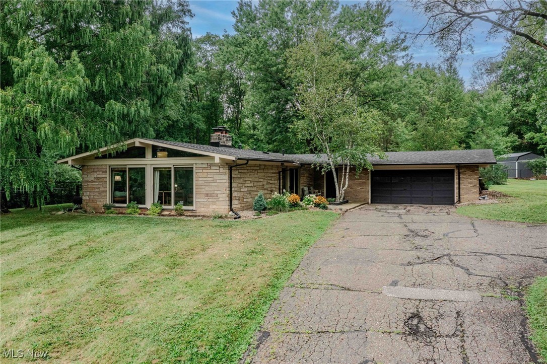 Every once in a while, you come across a life-changing home. Set on 1.39 acres in Bath, this mid-century modern ranch feels both timeless and refreshed, with every detail designed to connect indoor comfort to the beauty of the outdoors. Natural light spills through five sliding glass doors and gable windows, illuminating vaulted ceilings and reclaimed brick walls that anchor the home’s design. The open flow between living, dining, and kitchen areas makes daily life feel easy, while hardwood floors and granite counters balance warmth with sophistication. The kitchen blends style and function with stainless steel appliances, subway tile backsplash, and generous prep space. Just beyond, the living area opens to a shaded stone patio, the unmistakable centerpiece of the property. The primary suite offers space to recharge with dual closets, a beautifully updated bath featuring heated floors, and sliding doors that lead to the patio for morning coffee or evening stargazing. Two additional bedrooms carry the mid-century aesthetic forward with soaring ceilings and wall-length closets, while a second full bath keeps everything convenient. Practical upgrades mean peace of mind: roof (2019), washer and dryer (2020), whole-home generator (2021), gutters and guards plus masonry and flashing (2022), dishwasher and hot water tank (2023). The two-car garage connects through a breezeway with its own entrance, while a storage shed and new landscaping complete the exterior. Surrounded by mature trees in a quiet neighborhood, this home offers the rare combination of privacy and design integrity. With nearly an acre and a half of land, striking architecture, and thoughtful updates, it’s more than a house—it’s a lifestyle waiting to be lived.