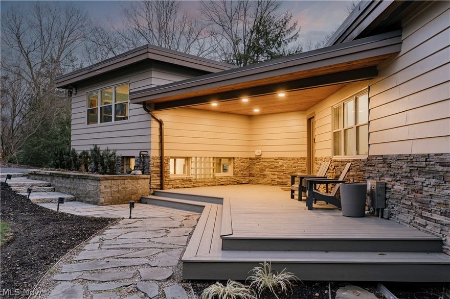 An exceptional modern retreat set on a serene, picturesque lot in Moreland Hills, where refined design meets effortless living. A winding, tree-lined driveway leads to a striking residence embraced by nature and a welcoming front porch—perfect for slow mornings and peaceful evenings. Inside, a light-filled open layout reveals architectural character at every turn. The living room is a true showpiece, featuring rich wood paneling, a dramatic brick fireplace, and expansive windows that frame the surrounding landscape, creating a warm, elevated ambiance. It flows seamlessly into an elegant formal dining room—ideal for intimate dinners. The kitchen is both stylish and inviting, centered around a generous island with breakfast bar seating—perfect for casual mornings, conversation, and connection. Sleek finishes, a tile backsplash, and a full suite of appliances are complemented by a cozy sitting area with a built-in desk, offering a comfortable space to work or unwind. Upstairs, the private quarters offer a tranquil escape. The primary suite is a peaceful retreat with a spacious bedroom, multiple closets, and a well-appointed ensuite featuring a double vanity and a large step-in shower. Two additional bedrooms and a full bath provide flexibility for family or guests. The lower levels expand the lifestyle even further, offering a spacious recreation room with kitchenette—along with a full bath, laundry area, and a versatile bonus room ideal for a fitness space, studio, or private office. Outdoors, the experience becomes truly exceptional. The backyard unfolds as a private sanctuary, where a sprawling patio invites effortless entertaining and everyday relaxation. Enjoy evenings in the partially covered hot tub, gather around the built-in BBQ and firepit, or simply take in the peaceful views of the wooded valley beyond. A home where comfort, style, and nature come together in one of Northeast Ohio’s most desirable settings.