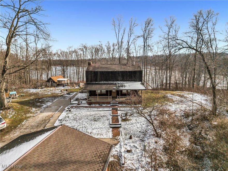 Situated on a 4.76-acre lot & sits on 500ft of frontage to the Mogadore Reservoir this 2-story, 5 bedroom, 2.5 bath home is the perfect retreat from the hustle & bustle of everyday life. Surrounded by shade trees, a picturesque backdrop at the water's edge, access to the Buckeye Walking Trails, & an abundance of natural wildlife, a paved walkway guides you to the large, covered front porch with swings, setting the tone for the welcoming ambiance that awaits you inside. Indoors, be greeted by an interior that exudes a cozy cabin feel, highlighted by stunning hardwood floors, exquisite natural woodwork, striking log beams that grace the ceiling & many windows providing views from every room that enhance the connection to the beautiful surroundings outdoors. The floor plan creates a seamless flow between the living, dining, & kitchen, making it perfect for entertaining. The living room boasts a wood burning fireplace with gas starter for ease of use. The island kitchen, with cooktop, features ample cabinet & counter space plus pantry, along with essential appliances including a double wall oven. Ascend the open staircase from the living room to discover a generously sized master, designed to accommodate various furnishings with an abundant amount of closet space. The other 3 bedrooms are also well-proportioned & carpeted for comfort while a conveniently located full bath features a separate shower & classic clawfoot tub. The basement offers additional living space with 1 finished bedroom, a sizable rec room, & full bath. The laundry & mechanical room, complete with washer & dryer, ensures practicality for everyday living. A spacious rear deck overlooks the tranquil waters, perfect for enjoying leisurely mornings with a cup of coffee or take a break and fish, kayak, boat, or hunt(in season) right from your own backyard. Additional features include a commercial hot water tank, detached 3-car garage, greenhouse, & animal barn, all contributing to the home's functionality.