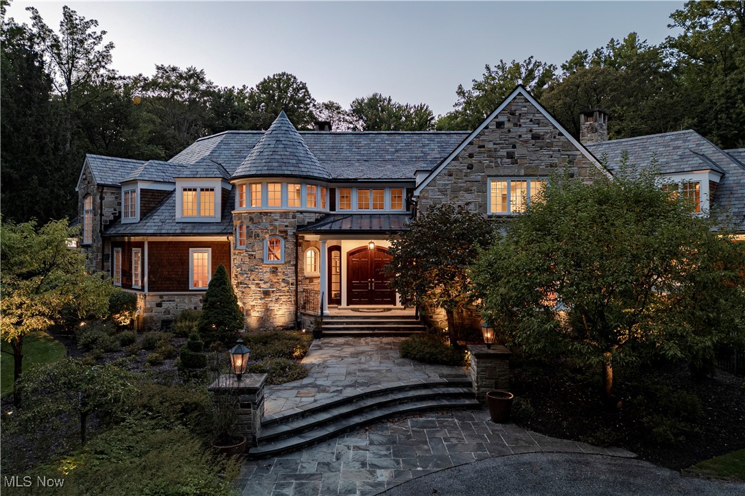 Set upon more than five acres of secluded, wooded grounds, this extraordinary Tony Paskevich designed French Country residence embodies timeless elegance, uncompromising craftsmanship, and countless thoughtful renovations. A private retreat of remarkable beauty that blends classic design with modern luxury. Double doors open to a grand foyer with a sweeping spiral staircase. The family room captivates with a coffered ceiling, custom built-ins, and a graceful bow window framing serene views, while a charming fireplace adds warmth. The living room impresses with soaring ceilings, refined millwork, a sandstone fireplace, and direct terrace access. The kitchen is both a culinary haven and a gathering space, featuring a center island, custom tile flooring, stone counters, two sinks, and an expansive walk-in pantry. A circular breakfast nook bathes in natural light, while the formal dining room—with bespoke wood built-ins and extraordinary windows—provides the perfect stage for memorable entertaining. The first-floor primary suite offers a world of its own, featuring dual walk-in dressing rooms each with its own washer and dryer, an elegant ensuite bath, and a private staircase to a secluded bonus retreat. Additional main-level highlights include two powder rooms and a studio with private elevator access. Upstairs, four ensuite bedrooms and a spacious studio/flex area provide comfort and versatility. The lower level is equally impressive, with a private bedroom suite offering fireplace and kitchen access, a state-of-the-art theater, an exercise room, and a luxurious sauna. Outdoors, the estate is nothing short of enchanting. Meticulously designed gardens frame two fountains, while mature trees and manicured beds create an atmosphere of serenity. A sparkling pool, spa, and multiple patios provide an idyllic backdrop for both intimate gatherings and grand celebrations. A rare masterpiece, this estate is more than a home—it’s a lifestyle of elegance and privacy.