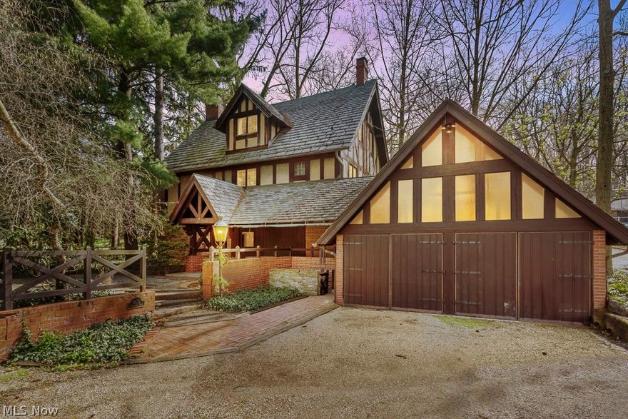 Step back in time to 1917 when Stan Hywet was the only house in the area. This unique “Poultry Keeper’s Cottage” was an outbuilding of Stan Hywet and the heart of the Sieberling Poultry Farm, housing the estate’s groundskeeper and gardener and storing feed for the birds. The brick Tudor home is situated on a lush corner lot planted with seventy-year-old evergreens and a stately dawn redwood.  The house offers all the charm, character, and quality construction of Akron’s boom-time, including natural oak woodwork, oak flooring on its 2nd and 3rd floors, built-in cabinetry, and some original bathroom fixtures. This property was lovingly renovated in the 1950’s to be a family home by world-renowned designers and preservationists F. Eugene and Ramona DeLaney Smith, who raised three children and resided there until present day. The custom-built kitchen has a timeless design with butcher block tops and stained glass cabinets. Floor-to-ceiling windows and a copper-topped fireplace are the focal point of the cozy living room, where morning light streams in from the east. The upper two floors, which were the original residence, hold five bedrooms, two bathrooms with cast iron tubs, and a library with oak shelving built over an entire wall. A breezeway-attached 2-car garage, added as part of the mid-century renovation, has a large storage area on its upper level. The west-facing porch, also constructed during the renovation, is an airy place to have a morning coffee or unwind later in the day and dine al fresco. The large brick patio is a quiet space for listening to the whispering trees and melodic birds. The whole property is blanketed with lush ivy and pachysandra, so there is green year-round and no grass to mow. Architect Charles S. Schneider and his builder, Mr. Palmer, designed and built the Poultry Keeper’s Cottage in 1917, two years after the Seiberling family moved into the manor house. The building was one of the first Tudor Revival structures in the city of Akron.