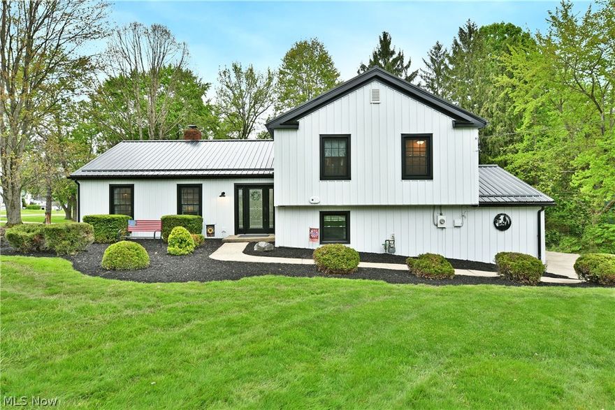 If you’ve been waiting for “the one” in Garrettsville—this is it! This masterfully renovated split level showcases an endearing, three-bedroom layout that’s sure to impress. A curb appeal champion, the home takes full advantage of its prominent corner lot, standing out from the crowd with its incredible, black and white steel exterior surfacing to include the siding and roof. This high contrast look exudes quality with long lasting style, all accented by manicured mulch and stone beds that hide multiple patio spaces that includes a covered and elevated rear section for warm summer evenings. Inside, the glass laden entry door opens to the welcoming foyer. Hardwood style flooring runs underfoot by the coat rack and continues into the fantastic living room where a large fireplace joins the lattice lined windows and illustrious recessed lighting. Around the corner, enjoy your favorite meals in the formal dining area, overseeing the window lined rear family room and its tall ceilings that join towering shelving for a perfect home office, study or home library. The central kitchen brings the heat with striking, butchers block countertop surfaces and artful lighting choices that pair with updated cabinetry and a hidden pantry. Upstairs, revel in the master suite and its custom private bath, brimming with stone and glass work. Two additional bedrooms accompany a brightly lit full bath while second floor laundry services end the hall. Down at the lower level, hidden utility access joins a half bath while a walk-out family room enjoys its stained wood built-in cabinets. Recent updates include 50-year metal roof installed 2023, 50-year board and batten metal siding 2023, vinyl windows 2023, seamless gutters and gutter guards 2023, bathroom and kitchen remodel 2025 and many more! Prime location near the library, schools, Village park, Headwater Trail and Village Business District.