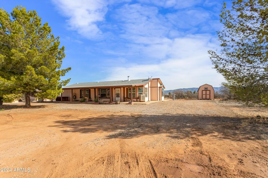 Welcome to your own slice of paradise! Nestled on just under 4 acres of land, this charming manufactured home boasts breathtaking views in every direction. The property is fully fenced and crossed fenced, providing privacy and security. Step inside to discover a cozy yet spacious interior featuring 3 bedrooms & 2 bathrooms. Enjoy convenience of an eat-in dining area as well as formal dining room, perfect for entertaining or hosting family dinners. Outside, you'll find three sheds and 2 car garage offering ample storage space. Enjoy the Arizona sunsets on your large covered porch over looking the mountains while in your rocking chair or hot tub also on the porch. RV parking on North side of house with hookups.