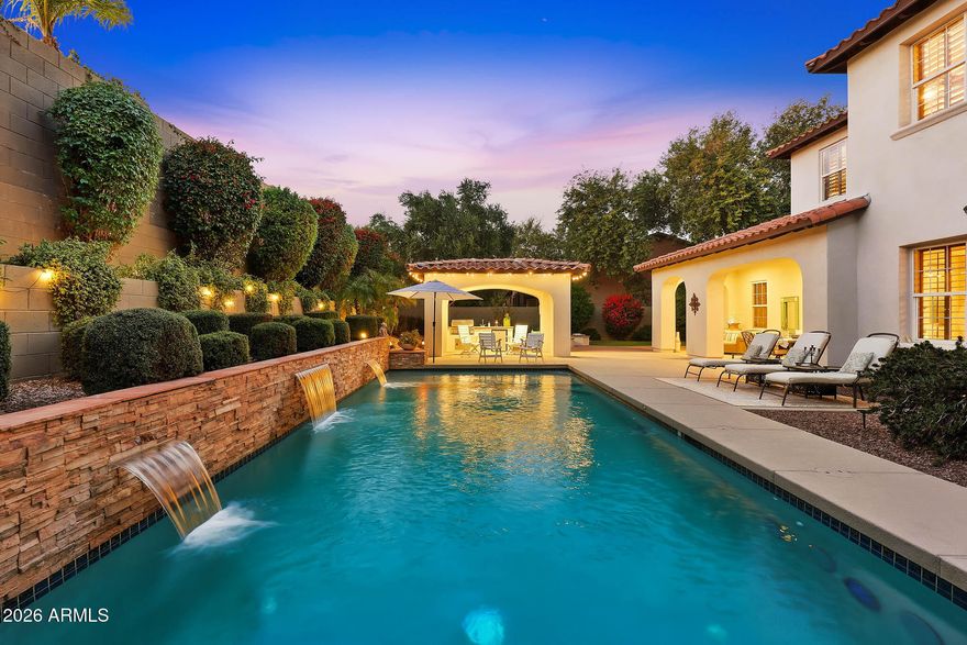 Discover this gorgeous Spanish Colonial two-story residence ideally located in the heart of Verrado's Main Street District. Offering 4,052 sq ft of thoughtfully designed living space, this home features 4 bedrooms, 3.5 bathrooms, and a versatile floorplan including a formal living room, dining room, private office, spacious family room, and a fully equipped kitchen - perfect for both everyday living and entertaining. Every detail reflects exceptional pride of ownership, from the striking custom brick archway entry to the hand-scraped wood floors, beautiful cabinetry, and classic plantation shutters. From the moment you step inside, the home exudes warmth, cohesion, and timeless design, creating a space that feels both elegant and inviting. Step outside to a private outdoor retreat, a secluded desert oasis designed for unforgettable gatherings. Enjoy a sparkling pool, lush mature landscaping, an expansive covered patio, ramada with built-in BBQ, fire pit, and low-maintenance artificial turf; an ideal setting for relaxing evenings and entertaining family and friends. Upstairs, spacious bedrooms are anchored by an oversized primary suite complete with a sitting area and a spa-inspired bath featuring a soaking tub, dual vanities, and a generous walk-in closet. An additional ensuite bedroom, along with two more bedrooms and a shared bath, completes the upper level. Living in Verrado means enjoying iconic tree-lined streets, over 86 parks, championship golf, A-rated schools, and the upcoming Vestar outdoor shopping and dining district, slated to open in 2026 with shops, restaurants, and a movie theater. Experience the lifestyle that makes Verrado one of Arizona's award-winning master-planned communities. Schedule your private tour today and see firsthand everything this remarkable home has to offer.