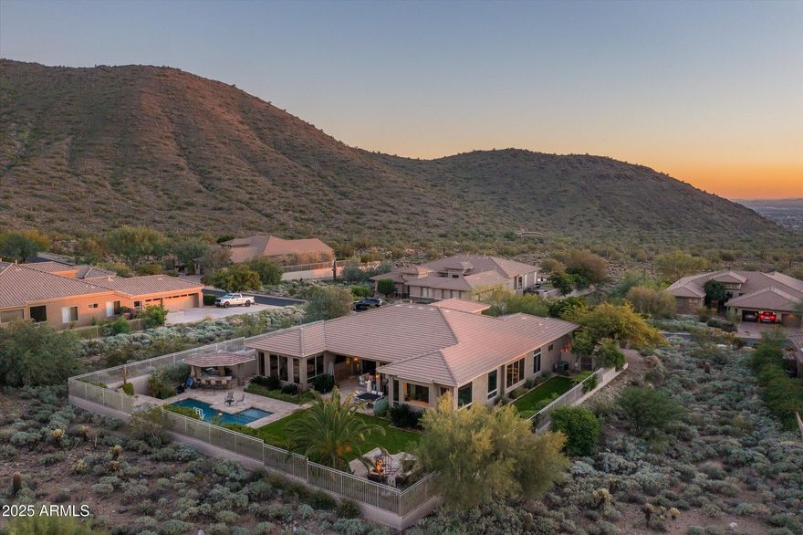 Situated on one of the premier lots in Sonoran Estates II, this home offers exceptional curb appeal with a welcoming front courtyard and built-in firepit. Sweeping canyon and mountain views and breathtaking sunsets create a striking first impression as you enter the formal living and dining rooms.  A recent remodel showcases a stunning kitchen with all new appliances, a large quartz-slab center island, and a built-in Sub-Zero refrigerator. The kitchen flows seamlessly into the breakfast nook and great room, where walls of windows frame the backyard and surrounding mountain ranges. The outdoor living space is designed for year-round entertaining, featuring telescoping doors that open to a deep covered patio, resort-style pool and spa, and a fully equipped outdoor kitchen with gas grill, griddle, beverage station, lighting, and surround sound. An elevated seating area with a firepit overlooks the canyon, offering a perfect setting to take in sunset views. The primary suite is a private retreat with direct backyard access, a spacious walk-in closet, and a newly remodeled spa-style bath with an oversized shower and steam room. An en-suite guest bedroom with private bath and walk-in closet is located on the opposite wing, while three additional generously sized bedrooms and a bath are thoughtfully positioned nearby.
Set on nearly one acre, the property offers exceptional privacy and dramatic desert surroundings.