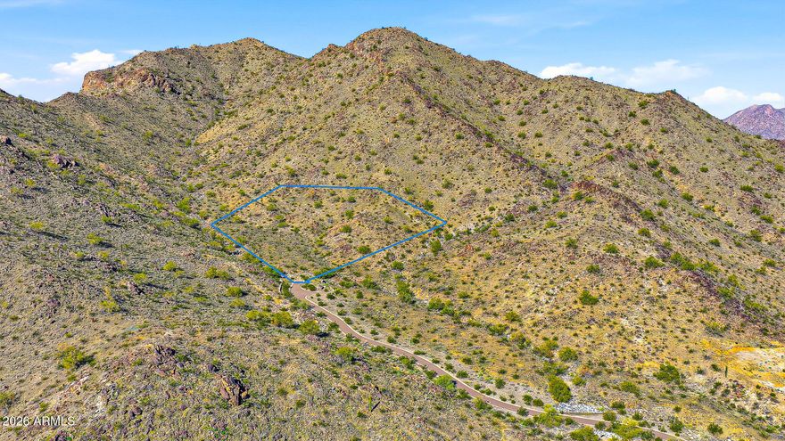Some seek the convenience of being close to town—shopping, schools, dining, and entertainment just moments away. Others are drawn to wide-open spaces, where nature provides peace, privacy, and inspiration. At the custom enclaves of Verrado, you no longer have to choose. Homesite #1 is nestled within the exclusive Mountain Coves Enclave of Verrado, located at the base of the White Tank Mountains and accessed by a secluded private driveway, offering exceptional privacy and serenity. Ever dreamed of owning your own personal mountain? Spanning an impressive 5.09 acres, this expansive mountainside homesite delivers a rare opportunity to do just that. Surrounded by the breathtaking beauty of the Sonoran Desert, the property perfectly complements Verrado's charming, tree-lined streets and small -town ambiance. The community features over 80 parks and greenbelts, ensuring every home is within two blocks of open space. This premier homesite showcases sweeping panoramic mountain views, sparkling city lights, and unforgettable Arizona sunsets. Verrado is further distinguished by two Tom Lehman-designed championship golf courses, a vibrant City Center with shopping, dining, fitness facilities, and pools, as well as highly rated A-schools. With an active calendar of clubs, events, and amenities, Verrado offers something for every lifestyle. This extraordinary homesite is an ideal canvas for a custom dream home and is sure to impress even the most discerning buyer. Experience the Verrado lifestyle.