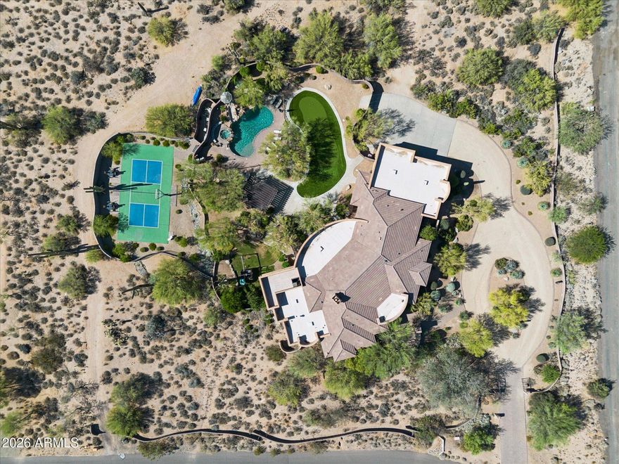 BRONCO. A privately gated 2.5+ acre estate in North Scottsdale. 6,300+ square feet of custom construction where the materials do the talking: hand-hewn log beams, travertine & hand-scraped wood floors, stone work, solid wood furniture-grade cabinetry throughout. Warm desert tones. Authentic Southwest architecture, built with intention. The main floor is organized around how people actually live. A commanding great room with dramatic ceiling detail & statement fireplace wall opens to the chef's kitchen with gourmet appliance suite, two dishwashers and an expansive island with breakfast bar. The split primary suite occupies its own wing offering generous space & privacy with direct access to the outdoor living areas. A front guest suite, three additional guest rooms, two full baths and den give the house genuine flexibility for families of any configuration. Formal dining, breakfast room, office or game room & half bath complete the main level. The basement operates as a fully independent layer: living room with kitchenette & bar, pool table room, sixth bedroom & full bath. Multigenerational households, long-stay guests and extended family can all land here comfortably. Outside, the property earns its reputation. Wrap-around covered patios connect interior living to the grounds at every turn. The front fireplace courtyard announces the arrival. Out back: heated pool & spa with water slide & grotto, pergola with fireplace, outdoor kitchen & outdoor shower. Newly installed pickleball and sport court, five-hole putting green and children's playground fill the acreage. Minutes from Scottsdale's top dining, shopping, and the McDowell Sonoran Preserve trailheads. BRONCO carries a documented short-term rental history with strong financials available to qualified buyers. This special property is equally compelling as a primary residence, second home, or income asset.