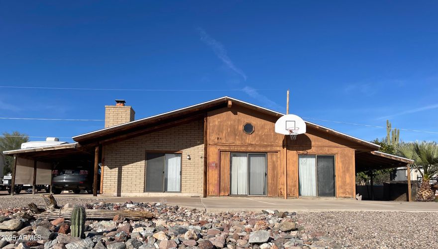 The uniqueness of this home is charming. County records has this 2 bedroom (loft+), 1 bath home as a single family residence located in the manufactured home area of Queen Valley. The stick-built home was built around a manufactured home which was removed after the building was finished. Step inside to a cozy living room with a working wood burning fireplace. The galley kitchen opens into the living room. There are two areas being used as bedrooms located in the loft, and two bedrooms on the main level. The furnishings in the home stay. The two car garage can be accessed via the alley behind the home or the right side of the home. There are two car ports. There is a laundry shed with storage and another shed for your hobbies. Play ball on your own half court.  Queen Valley has no HOA.