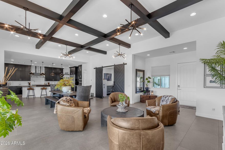 Welcome to an entertainer's dream where architectural intention meets everyday livability. Soaring 12-foot coffered ceilings crown both the great room and formal dining, while a dramatic 20-foot sliding glass wall dissolves the boundary between indoors and out, creating a seamless indoor-outdoor flow designed for gatherings that linger long past sunset. Throughout the home, 10-foot ceilings and curated, design-forward finishes elevate every space. The living area is grounded in large-format concrete-look porcelain tile, creating a sleek, architectural foundation, while thoughtful details like faux wood beam accents layer in warmth and dimension--balancing the home's modern aesthetic. Two expansive living spaces offer the flexibility to host with intention or unwind in a more relaxed setting.

At the heart of the home, a true showpiece: a chef's kitchen that doesn't just function... it performs. Outfitted with stacked cabinetry, soft-close millwork, and a striking leathered granite oversized island, the space is elevated by a full-height glossy backsplash in a clean stacked layout, delivering a polished, modern edge with just the right amount of shine. Premium Monogram Appliances take center stage, including a commanding 48-inch gas range with pot filler, double ovens, and a built-in wine refrigerator--because entertaining should feel effortless, not limiting.
A set of sliding barn doors reveals a private office or den, offering flexibility without sacrificing style.

The primary suite is a retreat in every sense, featuring generous proportions, a spa-inspired bathroom, and an expansive walk-in closet designed for both function and indulgence.

Beyond the main living areas, a thoughtfully designed secondary living wing creates its own private enclave, complete with a separate living room/den that anchors the space. En-suite bedrooms and this living area enjoy private access to a serene courtyard, creating a tucked-away escape ideal for guests or multigenerational living.
Step outside to an oversized lot with no rear neighbors, already prepped with gas and electric for a future pool. For now, unwind in your private spa and cold plunge, or gather around the gas firepit under the Arizona sky--where evenings stretch a little longer and life slows down just enough.
Located within The Estates at Eastmark, residents enjoy access to a private clubhouse complete with a pool, firepits, lounge areas with TVs, a fully equipped workout facility, and a kitchen designed for hosting and connection. Beyond that, the greater Eastmark community unfolds with the Great Parks, featuring a splash pad, play structures, a lake with a riparian stream, event pavilion, open fields, scenic paths and trails, a skate park, and an 18-hole disc golf course.
With highly rated schools for all grade levels, a new 30,000 sq ft library, and close proximity to shopping, dining, Queen Creek Village, Legacy Park, Mesa Gateway Airport, the 202 freeway, and the scenic beauty of Canyon Lake, the lifestyle here is as elevated as the home itself.
This isn't just a home... it's a stage for connection, celebration, and effortless luxury living.