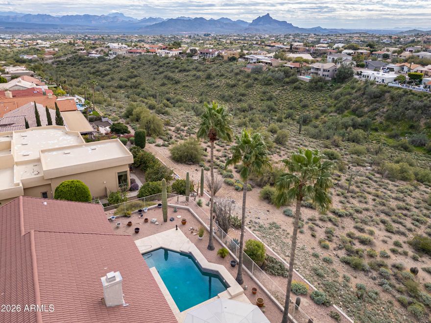 Gorgeous single-level home with outstanding views and great curb appeal. Enjoy Fountain and Four Peaks views from the front and Red Mountain and canyon views from the back, all on a private lot backing to a wash. This 2 bedroom, 2.5-bath home features a desirable split layout with dual primary suites plus an office with built-in desk system. The open-concept kitchen and family room offer vaulted ceilings, a fireplace, and a wall of windows and sliding doors that frame the backyard views and bring in abundant natural light. The kitchen is well-appointed with granite countertops, ample cabinetry, center island, breakfast bar seating, eat-in nook, and a bar area with fruit sink. A formal dining area adds flexibility for entertaining. The main primary suite includes a sitting area and direct backyard access with a security screen door. The en suite bath offers dual vanities, soaking tub, dual-head shower, and walk-in closet. Door to laundry room thru hallway and master bedroom closet. The second primary suite features dual vanities with makeup station, jetted tub, separate shower, and walk-in closet. Additional highlights include plantation shutters throughout, solid interior doors, travertine and Berber carpet flooring, a spacious laundry room with sink and storage, and double front entry doors with security screen for fresh-air living. The backyard is designed for low-maintenance enjoyment with a heated and chilled PebbleTec pool, extended covered patio, multiple seating areas, and exceptional privacy. The 2-car garage includes epoxy floors, built-in cabinets, and a side service door. Furnishings available by separate agreement.