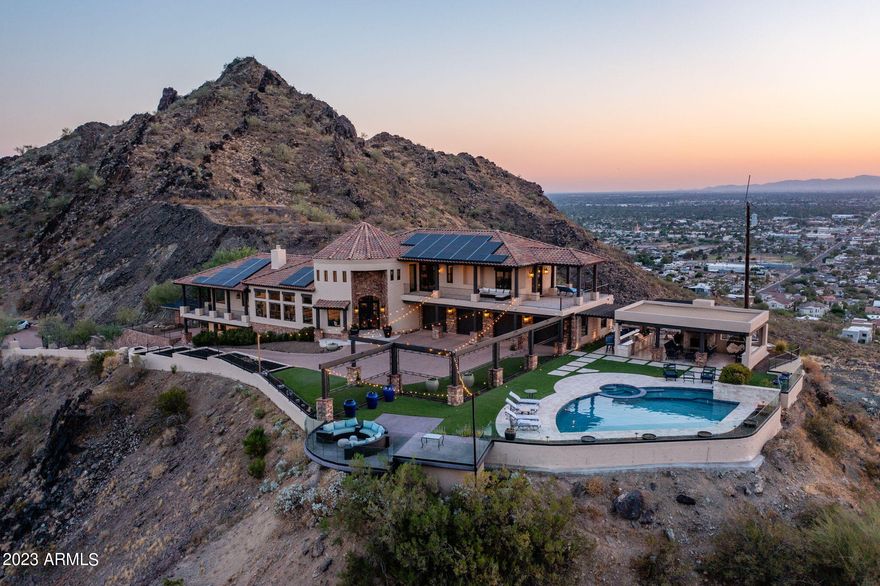 This stunning mountainside estate boasts jaw dropping 360 degree views that are unrivaled by any other property in the city. Situated on nearly 3.7 acres on the edge of the Phoenix Mountain Preserve, the city and mountain views are everchanging and include Dreamy Draw, Piestewa Peak, Lookout Mountain, North Mountain Park, Downtown Phoenix, Phoenix Sky Harbor, Chase Field, and all the way to the State Farm Stadium. As one of the highest elevated homes in the Valley, the seclusion and privacy of this property all while being centrally located in Phoenix is extremely rare. Every room of the home takes advantage of the mesmerizing mountain views. The living area has 12 foot ceilings, is filled with natural light, has hardwood floors, and a floor to ceiling natural stone fireplace. The chef's kitchen features knotty alder cabinets, quartz counters, marble backsplash, a large island, and top of the line appliances with a Wolf Range, Wolf double ovens, Subzero refrigerator and freezer, Cove dishwasher, Viking built-in microwave, a commercial ice maker, and a multi-filtered Kinetico water system. The primary suite has city and mountain views, a wrap around private balcony, two walk-in closets, blackout motorized shades, and hardwood flooring. The primary bathroom has a soaking tub with a chandelier, dual sinks, and walk in shower. Both guest bedrooms upstairs are en suites, have huge walk-in closets, hardwood flooring, plantation shutters, and access to a 900 square foot balcony. The bottom level has two additional bedrooms, laundry, storage, and another private patio. The driveway is over 7,500 square feet of paver stone with multiple parking areas, and there is a 4 car garage with an EV charging station, extra storage cabinets, and a central vac system. The outdoor living is an incredible space that has a kitchen with granite counters, stainless grill, bread warmers, and sink. There are multiple fireplaces, travertine flooring, tongue and groove natural wood ceiling, Sonos speaker system, misters for those hot afternoons, synthetic grass, and a glass surround wall to further take in the never ending views. The PebbleTec pool has a waterfall feature, new Pentair pump, spa, and is fully heated with a new Pentair heater. All 91 of the Tesla solar panels are owned outright with no balance and offer incredible electric bill savings that often result in a future credit.