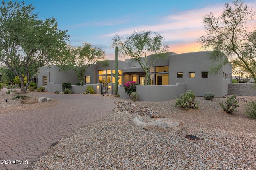 The warmth of this contemporary southwestern home is apparent from the moment you walk through the front door. Situated on a ¾ acre lot, with the arroyo running behind the home, you will truly feel as though you have found the perfect desert oasis. The mixture of textures - wood floors, stack stone brick fireplaces, wood cabinets, smooth coat walls, plush carpet and unique tile all come together to create a spectacular luxury home just waiting for you, your friends, and your family to enjoy. Creative architectural features and amenities are thoughtfully used throughout the home. The dining room ceiling feature enhances the area complete with a custom refrigerated wine display and is within steps of the amazing kitchen. Complete with a walk-in pantry, Monogram fridge, 48'' Monogram gas range, Monogram dishwasher, Monogram microwave drawer, pot filler, open shelving, and custom vent hood - it has it all. You'll never run out of counter space or cabinets, and with it opening to the charming family room (with a fireplace, of course!), this living area will be the place to gather for friends and family.  The primary bedroom boasts a fireplace with stack stone brick surround and a bathroom with steam shower and has its own access to the backyard. Nothing was missed, from the metal pivot doors to the finished garage floor, you will see that the remodel was complete and high quality. The backyard has turf, a sparkling pool with water feature, heated spa, outdoor fireplace, covered patio, and built-in BBQ making it the ideal place to be regardless of the time of year. Years of stunning sunsets and starry nights will be yours to enjoy with this beautiful home.