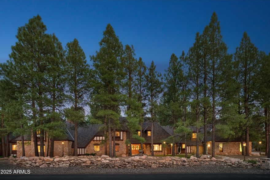 Nestled in the quiet embrace of the pines in one of Flagstaff's most iconic country club communities, this timeless Tudor-style estate offers a rare kind of presence, enduring and quietly majestic. The 7,700+ sqft home on 1.32 acres was designed not for trend, but for timelessness. With 8 bedrooms and 5 baths, it's more than a residence; it's a retreat, a gathering place, a sanctuary ideal for hosting extended family, welcoming friends, or creating a true multi-generational residence. From the moment you enter, there's a sense that this home has held many winters, many stories. Exposed wooden beams stretch across high ceilings, grounding the space with warmth and character along with two inviting floor to ceiling stone fireplaces. Rich wainscoting lines the walls throughout the home, adding depth, texture, and a sense of refinement. Built-in window seating offers cozy corners for reading, dreaming, or simply watching the seasons pass. A wonderfully updated modern kitchen, complete with high-end finishes and clean functionality, is seamlessly incorporated into the existing space offering the best of both worlds: timeless design with today's ease. A spacious living room and a theater room are thoughtfully designed to blend effortlessly into the home's natural rhythm. The 2,200 sqft first floor master suite lives like its own private lodge, complete with a full kitchen and game room, perfect for long visits or multi-generational living.
And then there's the outdoors. Step outside under the pines and you'll find the magic continues. Tiered brick paths lead you through the landscape, revealing a peaceful waterfall pond, thoughtfully placed patios, and a built-in grill perfect for mountain evenings with friends and family. Follow the path a little further, and you'll discover a remarkable lower-level terrace anchored by a handcrafted wood-fired pizza oven.
For those seeking space for passion and purpose, the 7-car garage spaces and additional workshop are a dream come true. Whether you're a collector, a craftsman, or an artist in search of a creative haven - this space is more than storage; it's an invitation to build, restore, and dream. And while the home is move-in ready, it also offers room for vision. This is a home that can be loved as it is or elevated further. The possibilities are endless. A legacy property ready to be found.