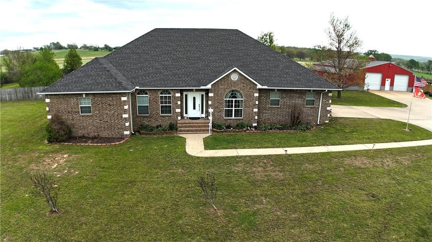Beautiful custom brick home on 5.7 acres just minutes from town! A concrete drive leads past newly planted pecan, apple, peach & plum trees to the home & 60x60 shop. Offering 3,144 sq ft, this home features 3 bedrooms, 3.5 baths—each bedroom with a private bath—plus a large office with built-ins, a music/game room or 2nd office, & a second living area or 4th bedroom. Semi-open, split bd floor plan. Kitchen includes granite, an island workspace, gas range, double wall ovens, & huge pantry with garage access. Sewing room off the oversized utility room. Oversized bedrooms with walk-in closets. Hand-scraped hardwood & tile flooring. In-line propane water heater(6-yr). In-ground saltwater pool (4-yr liner, 2-yr cover) in privacy-fenced yard. Brick 10x16 storm shelter with electric. Shop includes 20x25 lean-to & 1,200 sq ft 1 bed/1 bath apartment-ideal for multi-generational living, in-law quarters, guests, or rental income. 17 mi to U of A in Fayetteville, 9 mi to Siloam Springs, & 15 mi to​​‌​​​​‌​‌​​​‌‌​​​‌‌‌​​‌​​‌‌​​​​ I-49.