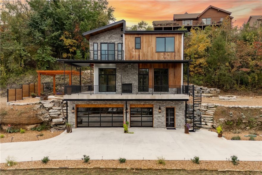 Perched above Beaver Lake, The Cliff House is a striking modern retreat that merges bold architecture with breathtaking views. Just minutes from downtown Rogers, and a public boat launch, this newly built home captures sweeping water vistas from nearly every room. The open-concept design features dramatic ceiling heights, clean lines, and curated finishes that showcase craftsmanship and creativity. At the heart of the home, the kitchen and living area share a dual-sided fireplace and open seamlessly to a full-length deckāperfect for entertaining or unwinding lakeside. But the showstopper lies downstairs: a hidden door disguised as a bookshelf reveals an incredible wine and cigar lounge built into the natural rock, complete with a secure vault door and custom lighting. Three bedrooms, three and a half bathrooms, a finished lower level, and a geothermal system complete this one-of-a-kind retreatāan architectural masterpiece designed to impress.