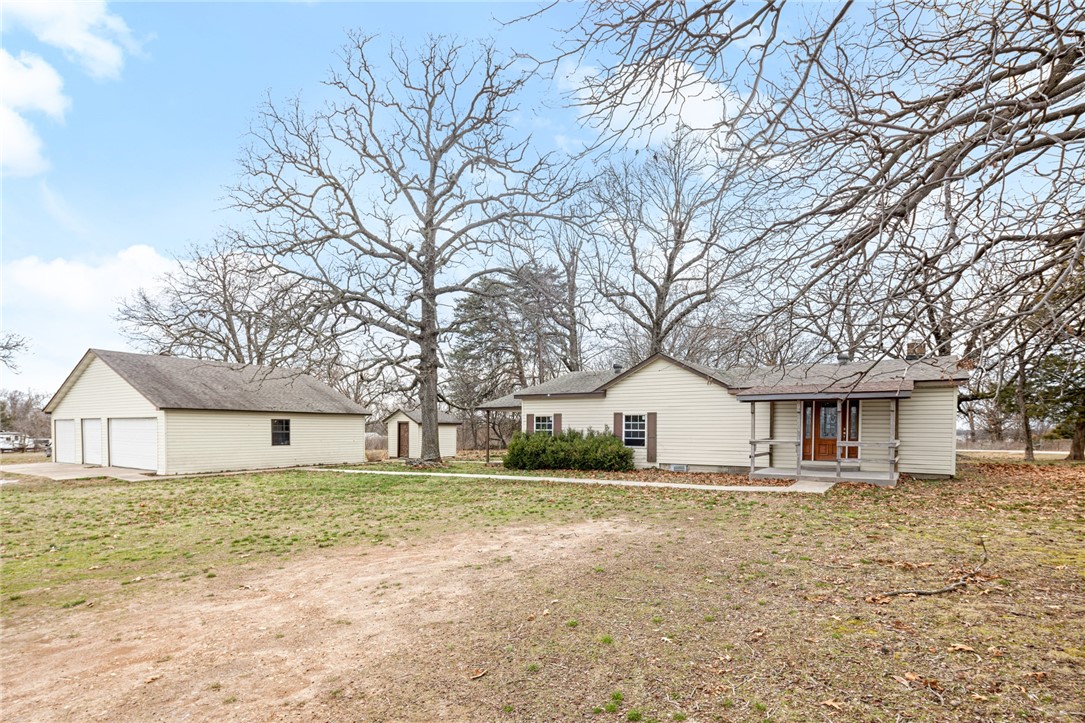 Home & 3AC & Detached Shop/Garage in Gravette! This property sits along Hwy 72 with great road frontage and easy access to town. The home features ample living space among its 1,864 sq ft layout. Spacious living room has large stone wood burning fireplace and wood floors. There is a flex space as well which is great for home office, playroom, additional living area. Large eat – in kitchen has ample cabinet and counter space along with electric oven and dishwasher. Primary bedroom has attached bath with whirlpool tub. Two guest bedrooms and a guest bath provide great space. The property also features a 39.8 x 29 detached 4 car garage with 110 electric hookup and 220 capable. There is also RV hookup on site. Enjoy plenty of space for gardening, homesteading, and more on your level, partially wooded 3-acre lot. Updates include new windows and trim. Property uses public water but has well on site and a 500-gal propane tank! Don’t miss this great find in NWA!