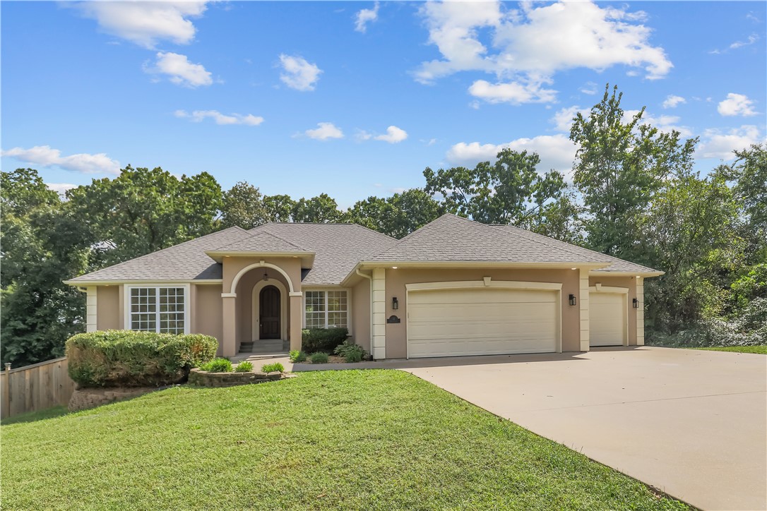 Welcome to 13 Shelly Lane, a beautifully updated 3,300-sq-ft home on two gently sloping lots in southeast Bella Vista. Built in 2006, this 3-bed, 2.5-bath property features a dedicated office and a spacious three-car garage with an epoxied floor and workshop area. The main level offers cathedral ceilings, a completely renovated kitchen with custom cabinetry and new granite countertops, and a serene primary suite with private access to a large upper deck overlooking the trees. Downstairs provides a second living room with an electric fireplace, a full kitchen with a built-in keg cooler, two additional bedrooms, and a full bath—ideal for guests or entertaining. Enjoy outdoor living on both the covered patio and the expansive deck, plus a charming treehouse that connects to the deck for added fun. With a newer HVAC system, plentiful upgrades, and 0.71 acres of peaceful privacy, this move-in-ready home blends comfort, space, and character.