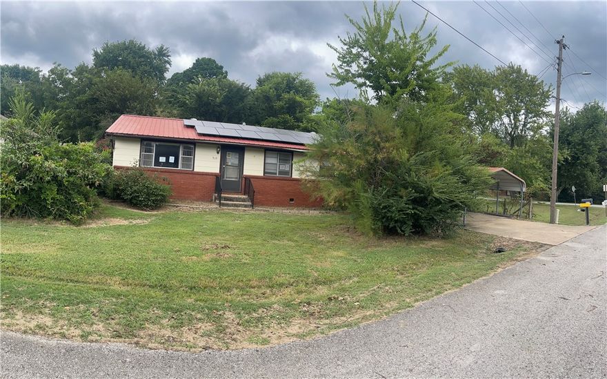 This home is a great example of a classic small-town property with timeless charm. Featuring a versatile floor plan, it can easily be converted into a mother-in-law quarters with kitchen access, a half bath, and direct entrance from the carport. The spacious lot offers plenty of room for a garden, storage shed, and a graveled area perfect for parking a vehicle or boat. Conveniently located near the park, shopping center, post office, gas stations, school, library, restaurants, and just a few miles from the University of Arkansas. Enjoy energy-efficient living with solar panels that cut utility costs, boost home value, and provide eco-friendly comfort.