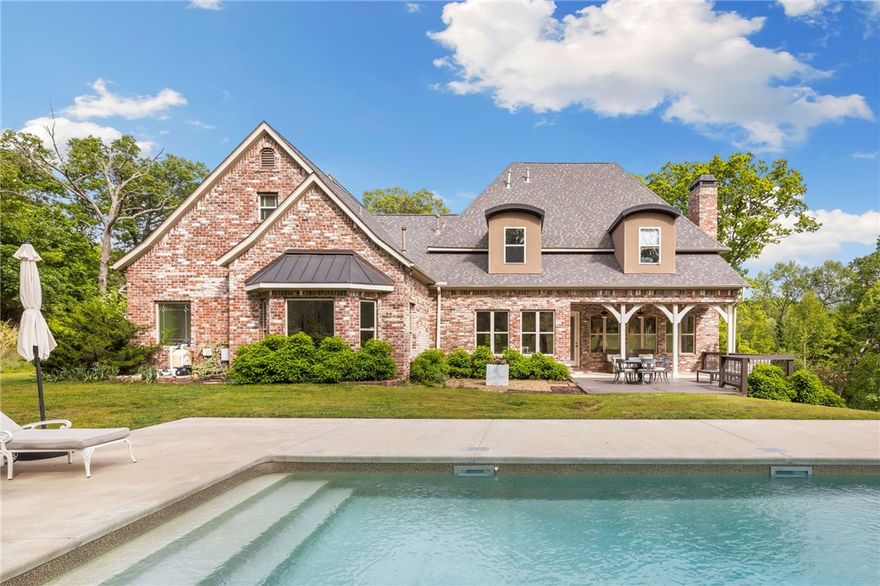 Nestled within the prestigious Talamore neighborhood, this exceptional brick estate offers the perfect blend of luxury & privacy on 5.81 wooded acres. The impressive 5,681 sq ft residence features 5 bdrms & 4.5 baths, all within the desirable Bentonville school district. Inside, you'll find soaring coffered ceilings, rich hardwood floors & custom millwork that speak to the home's exceptional craftsmanship. The gourmet kitchen features premium stainless appliances, striking black granite countertops & custom white cabinetry that flows seamlessly into bright, airy living areas w/multiple fireplaces. The spacious primary bedroom offers a private retreat with spa-inspired bathroom. Entertainment options are endless with a professional home theater, wet bar complete with wine frig, while outdoors beckons a resort-style pool perfect for summer gatherings. This extraordinary property strikes the perfect balance between elegant design & modern convenience, all while being conveniently located near Bentonville's amenities.