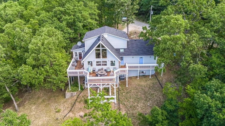 Secluded in a private, wooded setting with stunning mountain views, this mountain architecture with contemporary touches offers cathedral ceilings, skylights, and a gorgeous hand-blown light fixture that make the space shine. The main level features a bright kitchen, half bath, and living room that flows into a sunroom and half wraparound porch—perfect for year-round enjoyment. Upstairs, the primary suite offers privacy with its own en suite bath. The lower level includes two bedrooms, a cozy living area, and a warm shelter with stairs leading to a partially enclosed ground level—ideal for pets. Walls of windows fill the home with natural light, bringing the outdoors in. Just minutes from Eureka Springs, shopping, and Table Rock Lake, yet tucked away in your own peaceful mountain hideaway.