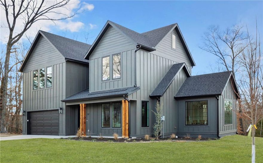 This thoughtfully crafted residence near Loch Lomond in Bella Vista stands apart with elevated design, refined materials, and attention to detail rarely found in today’s market. The striking exterior features modern architectural lines, vertical siding, and a cohesive palette that blends beautifully with the natural surroundings. Inside, wide-plank hardwood floors, soaring ceilings, and expansive windows create a light-filled, open atmosphere designed for both comfort and sophistication.  The kitchen is a true showpiece, offering custom cabinetry, a statement island with waterfall-style stone, designer lighting, and premium finishes that balance warmth and modern style. Seamless flow connects the kitchen, dining, and living areas, anchored by a tiled fireplace that adds texture and elegance. Every space reflects intentional craftsmanship, from trim details to thoughtfully selected fixtures. Minutes from Loch Lomond, trails, lakes, and golf, this home pairs elevated design with an outstanding Bella Vista lifestyle.