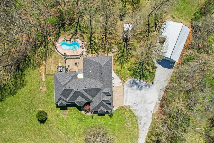 Experience the perfect blend of luxury, space, & privacy on 7.6 acres, approx. 15 minutes from downtown Bentonville. This home offers 5 bedrooms, an office, each main-level bedroom with its own private bath, & two living areas. The primary suite features a sitting area, dual-sided fireplace, & spa-style bath. Designed for everyday living & entertaining, the home includes two living areas, a bright sunroom, & a spacious kitchen with granite countertops. Step outside to enjoy the in-ground pool with waterfall, diving board, & deck overlooking the pool.  Recent improvements include interior paint (2026), updated lighting, new flooring, remodeled office bath, new pool pump, HVAC (2024), & a 2023 roof. The home also features a newly built 30x40 shop with private guest quarters including kitchen, living area, bedroom, bathroom, laundry, separate septic, & upstairs storage, ideal for guests or multigenerational living. A rare opportunity to own a beautiful property with acreage, pool, and guest house with shop.