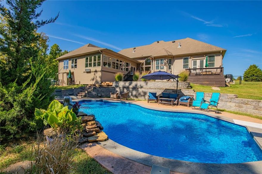 Experience the perfect blend of luxury, space, & privacy on 7.6 acres, approx. 15 minutes from downtown Bentonville. This home offers 5 bedrooms, an office, each main-level bedroom with its own private bath, & two living areas. The primary suite features a sitting area, dual-sided fireplace, & spa-style bath. Designed for everyday living & entertaining, the home includes two living areas, a bright sunroom, & a spacious kitchen with granite countertops. Step outside to enjoy the in-ground pool with waterfall, diving board, & deck overlooking the pool.  Recent improvements include interior paint (2026), updated lighting, new flooring, remodeled office bath, new pool pump, HVAC (2024), & a 2023 roof. The home also features a newly built 30x40 shop with finished living space, including kitchen, living area, bedroom, bathroom, laundry, & upstairs storage, ideal for guests or multigenerational living. A rare opportunity to own a beautiful property with acreage, pool, and guest house with shop.