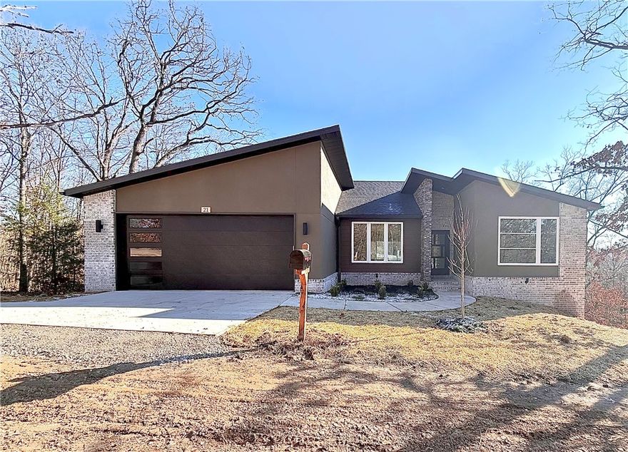 Move-in ready new construction by Elite Thomas Homes! This modern design features a sloped roofline with stucco, stone, and wood accents. Located on Bella Vista’s desirable east side, with the Taylor Homestead bike trail just behind the property. Large windows throughout the home capture beautiful wooded views from both levels. The main level offers an open living/kitchen/dining area with vaulted ceiling and beams, stacked stone fireplace, white oak flooring, and abundant natural light. The spacious primary suite includes a freestanding tub, dual vanity, tiled walk-in shower, and oversized walk-in closet. Bedroom 2 and a stylish guest bath complete the main floor. The partial walkout basement features a large media/game room, Bedroom 3, and a full bath, with premium upgraded carpet throughout. Two covered decks overlook the woods, giving you relaxing outdoor spaces to sip coffee, unwind at the end of the day, or entertain friends.