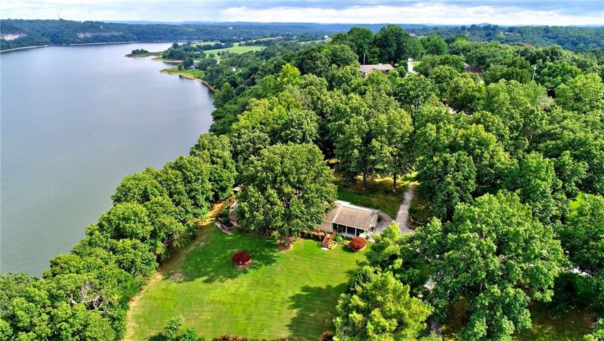 Stunning lake-view home on approx. 1.3 acres w/ panoramic views & boat slip on community dock included! 4BR/4BA, each w/ lake view & private bath—3 w/ separate exterior entrances, ideal for guests or STRs. Spacious primary suite opens to private balcony & upper deck—perfect for coffee at sunrise or wine at sunset. Basement BR has concrete block walls for storm safety. Enjoy the huge double stone patio, in-ground fire pit, fenced garden & raised beds. Skylights & solar tubes fill the home w/ natural light. Features include recirculating hot water, underground utilities, fiber internet, & storage building w/ power. Owned 1,000-gal propane tank fuels one furnace & freestanding fireplace; second HVAC is a heat pump. Propane is piped to front deck for grilling. Peaceful setting w/ the feel of a year-round vacation! Convenient to local restaurants, shopping, Fayetteville, & all that NWA has to offer.