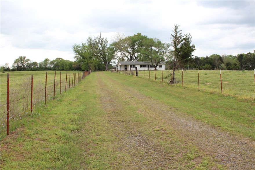 The property features well-maintained, fenced, and cross-fenced pastures. A cattle working lot is present and could be readily returned to use with some clearing. Amenities include a concrete waterer supplied by an existing well. Two ponds, stocked with fish, are located in the south paddock. A grazing lease is currently in place on the pasture, which is subject to termination or continuation by the new owner.
The residence is a well-maintained four-bedroom, two-bathroom home. It features a spacious living room and den area, with a combination of hardwood and vinyl laminate flooring. The entire interior has been recently repainted and is prepared for immediate occupancy. The exterior is finished with steel siding and includes a chain-link fenced area on the north side of the home. The yard is neatly kept, with Zoysia grass present in the front of the residence.
Also included is a one-car carport attached to the home.