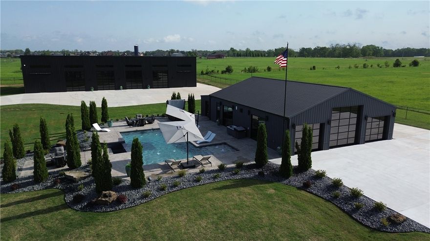 Stunning 2-bed, 2-bath Barndominium on 1.75 gated acres in Bentonville! With 2,456 sq ft of refined living and entertaining space, this custom barndominium features custom wood beams imported from Canada, a granite waterfall island with LED lighting and bar seating, a granite liquor display, epoxy floors, wine chiller, dual ice machines, premium A/V system, and a gorgeous fireplace. Two sliding doors and three electric roll-up doors (one 12’, two 8’) open to a resort-style saltwater pool with infinity edge, four fountains, sun shelf, color-changing lights, stamped concrete deck, outdoor speakers, and relaxing bubblers. A 50’x120’ upgraded metal building adds incredible value with polished concrete floors, 14’ Raynor doors, interior/exterior RV plug-ins, propane heating with wall-mounted controls, and spigots—one tied to irrigation. Professionally landscaped and thoughtfully designed, this property offers the ultimate blend of luxury, function, and entertaining space.