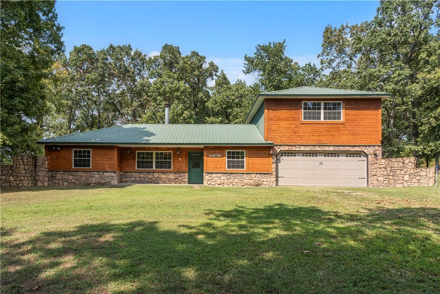 Escape to a private retreat just outside of Bentonville!This charming home is nestled on 5 acres of pasture and mature woods, offering the ideal balance of privacy and convenience.Step inside and you are welcomed by the warmth of a stunning two-sided stone fireplace, creating a cozy connection between the living and dining areas. The kitchen features knotty pine cabinetry, stainless steel appliances, and granite counters—perfect for everything from casual family dinners to entertaining friends.The spacious primary suite, privately located upstairs, offers a peaceful haven with its own deck overlooking serene country views. Two additional bedrooms provide comfort and flexibility for guests, family, or a home office. Outside, the land invites endless possibilities—from gardening to hobby farming to simply enjoying the countryside. If you’re seeking the peace of country living without giving up quick access to town, this property is the perfect fit. Bonus: The house is available next door for additional opportunities!