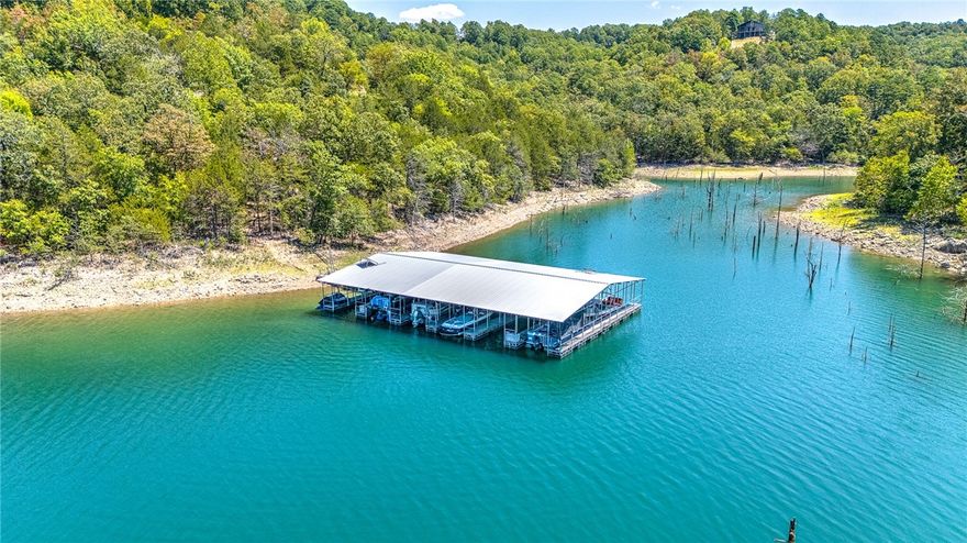 Stunning one owner custom-built masterpiece. Boat slip, lift, and Polaris side by side convey! Situated on 1.19 acres, the home boasts beautiful curb appeal, natural stone accents, and welcoming front porch. You’ll be dazzled by the beautiful hardwood floors, soaring ceilings, and panoramic views of Beaver Lake from each room. Office off the entry features coffered ceiling and built-ins. Kitchen is a chef’s dream with an oversized walk-in pantry, expansive countertops for food prep, a large island with built-in storage and seating, S/S appliances, and opens to a breathtaking screened-in porch. Multiple entertainment areas were designed creating access to the great outdoors. Primary Suite is expansive.  It showcases walk-in closet, laundry room, plus a luxurious en-suite bathroom. Family Room features a beautiful fireplace w/built-ins. Lower level includes multi-purpose room with kitchenette and separate heated & cooled workshop with extra storage. Custom features throughout. Whole house generator.  New roof (2024).