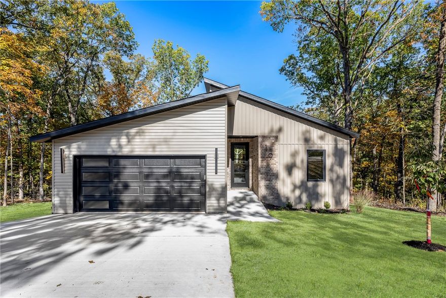 Located on the east side of Bella Vista with quick access to Pea Ridge and nearby bike and walking trails, this modern 1,900 sq ft home is tucked away on a quiet cul-de-sac and surrounded by mature trees, offering exceptional privacy. The open-concept layout features abundant natural light and seamless flow for everyday living and entertaining. Upgrades include luxury vinyl plank flooring, quartz countertops, built-in drawer microwave, and propane drop for gas range hookup. The living area features an electric fireplace and opens to an oversized covered back porch overlooking a gently sloping yard and surrounding hardwoods. Additional highlights include wiring for sound, pre-wiring for a security system, and a 1-year builder’s warranty for added peace of mind.