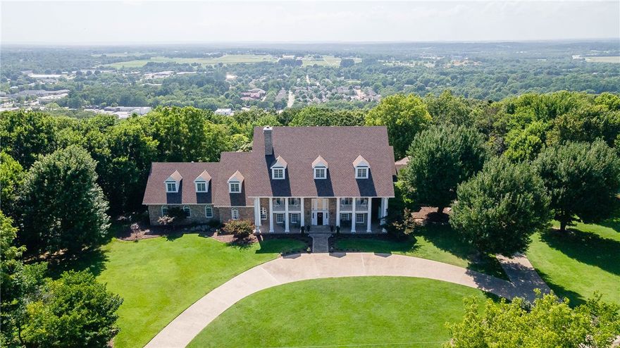 Charming estate property situated on 2.58 acres overlooking Fayetteville featuring a timeless brick and stucco exterior, grand columned entrance, circular driveway, mature landscaping, and expansive lawn. Centrally located near all that Northwest Arkansas has to offer, this home features 5 bedrooms plus an abundance of flexible living and entertaining spaces. Stunning outdoor areas include a diving pool, hot tub, and expansive patios and decks with breathtaking treetop views. Inside, elegant details shine throughout with wood floors, wood windows, custom finishes, open-concept living, and a centrally located kitchen offering abundant cabinetry and countertop space. Additional features include an elevator and endless opportunity to make this one-of-a-kind property your own.