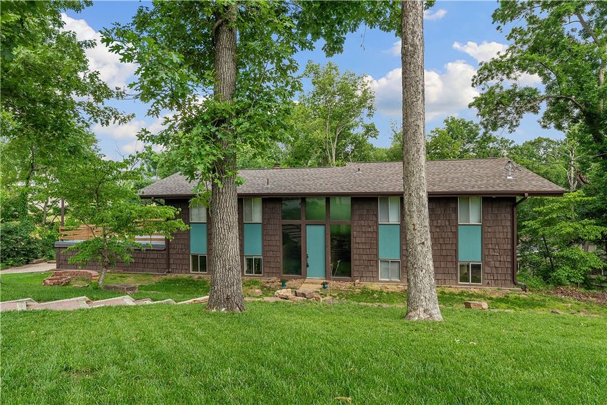 Welcome to Sherwood Forest—your serene, wooded cul-de-sac retreat backing to Coler Mountain Preserve with direct trail access & just moments from downtown Bentonville. This spacious mid-century modern split-level home on .41 acres offers privacy, mature trees, a peaceful creek & stunning views from multiple decks. Inside, enjoy vaulted ceilings, exposed beams, two wood-burning fireplaces & floor to ceiling windows. The main level has an oversized primary suite with en suite bath, double vanity, built-ins, walk-in closet & a giant family room. Downstairs, find a well-equipped kitchen with a double oven, wet bar, large pantry, formal dining, as well as, two additional spacious bedrooms. Other features include a central vacuum, intercom, dual-zone HVAC & no restrictive HOA. Recent updates: new roof, sodded yard, paved stairs, paint, carpet, fence & resealed patio. Bike straight to the HUB at Coler in 5 minutes, Slaughter Pen in 7 min, Walmart HQ, Crystal Bridges, The Momentary within 10 min ride—this home has it all!