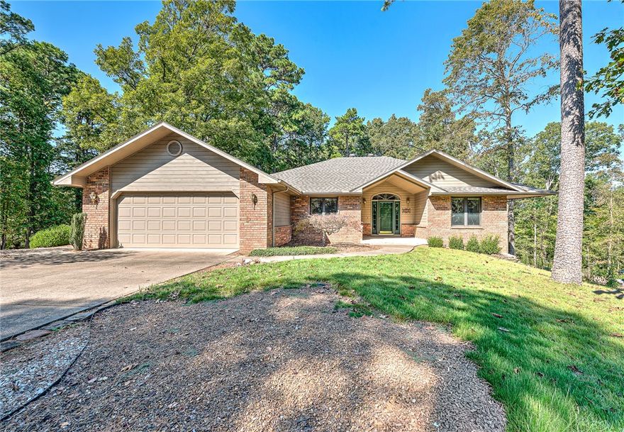 Located on a corner, flat lot close to Lake Rayburn, mountain biking trails and many Bella Vista amenities, this beautifully maintained 2 bedroom, 2 bath home with a dedicated office offers comfort, function and a natural setting on a nicely landscaped flat lot with rock and Zoysia grass. The house backs up to a peaceful POA wooded property. This home features an eat-in kitchen, laundry room with a sink and a generous primary suite with direct access to the covered deck.  The private office features glass doors--great for remote work or a quiet reading space. The oversized garage provides enough space for hobbies and there is an additional workshop located under the house is great for projects and extra storage.