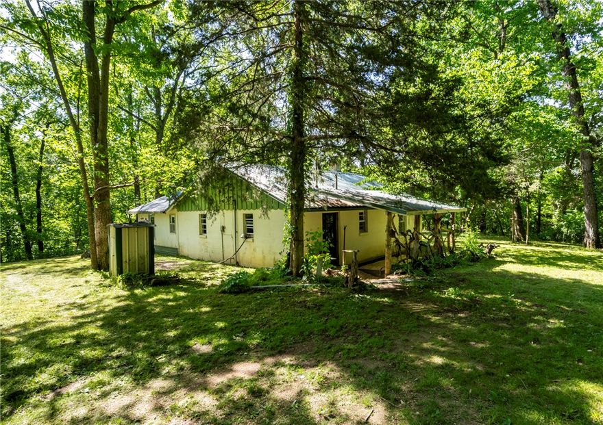 Located across the road from Rootville with frontage on Spavinaw Creek, this rustic, secluded cabin/house was built in the 1970s by the family who have owned this land for generations and the two story insulated metal outbuilding was added later. The 2 BR 2 BA house has electricity, septic, propane and a well on the property. The outbuilding could easily become a barndominium & is insulated with electricity. The 69.65 acres of pristine woods, 600 plus feet of creek access just below the house sits amid mature woodlands and beautiful low cliffs and rock formations making it perfect for recreational use. This property is located next to a private hunting and fishing recreational facility. The original concrete block house has a metal roof and is sturdy. It could be a retreat cabin or become the beginning of an amazing larger home. You will want to see this for yourself. The lines drawn are not a survey but an estimation of property boundaries. House and outbuilding sold as is.  Also see listing #1344875