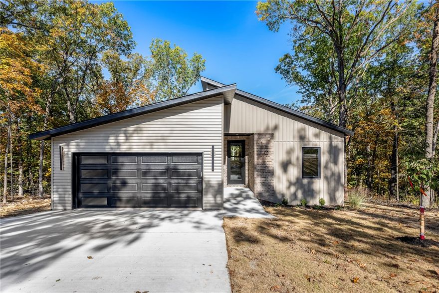 Located on the east side of Bella Vista with quick access to Pea Ridge and nearby bike and walking trails, this modern 1,900 sq ft home combines style, function, and privacy. The open-concept layout features abundant windows for natural light and a seamless flow throughout. Interior upgrades include luxury vinyl plank flooring, quartz countertops, built-in drawer microwave, and a propane drop ready for a propane range hookup. The living area offers an electric fireplace and access to a covered back porch overlooking the wooded surroundings. Home is wired for sound, prewired for a security system, and comes with a 1-year builder’s warranty for added peace of mind. This home sits on a quiet road surrounded by mature trees, offering the peace of the country with the convenience of nearby city access.