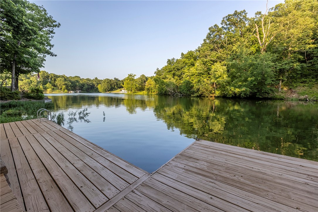 Park-Like, Secluded Lake-Front Living! 1.66 double lot with killer views and a private dock and covered boat lift. The oversized kitchen features granite counters, a double oven, gas cooktop, coffee station and massive amounts of storage. Throughout the upstairs, enjoy expansive lake views with 3 double doors accessing the deck and screened in porch. The upper living area has a propane fireplace while the lower level has a wood burning fireplace. In the primary bedroom + bath you'll find a private deck area, two walk-in closets, gorgeous marble double vanity, soaking tub, tiled shower and another walk-in closet. The laundry room has a sink with granite counters and even MORE storage. Downstairs you'll find 2 bedrooms, one full bath, and another living room/game room - the pool table conveys- and a wet bar to entertain your guests! Ice machine, sink + mini fridge in the downstairs bar convey as well. Brand new HVAC system in Jan 2024, Hot Water Tank 2019. New dishwasher in 2025. Lower level shop area + so much more!
