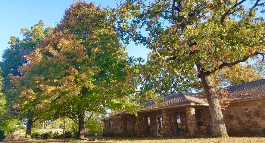 Set on 1.34 acres at the foothills of the Boston Mountain this charming rock home offers space and stunning views. Enjoy a large sunken living room complete with vaulted ceilings, a rock fireplace, Buck Woodstove, & cedar barnyard walls. The kitchen features stainless appliances, a double oven, farmhouse sink & a movable island. Relax on the new redwood-colored composite deck or the stenciled front porch surrounded by mature oaks, maples & fruit trees. The primary suite offers an ensuite, double closets & sliding doors to enjoy the backyard sunsets. Highlights include: Anderson windows & 2 sliding doors (installed in 2020), luxury vinyl flooring in the living room & kitchen & a large utility/laundry room with extra storage. Outside, find a chip & seal driveway, 2-car garage & a large workshop with a roll-up garage door & carport.  This property perfectly blends rugged mountain character with modern efficiency & serene natural views. Don't miss the chance to make it yours!