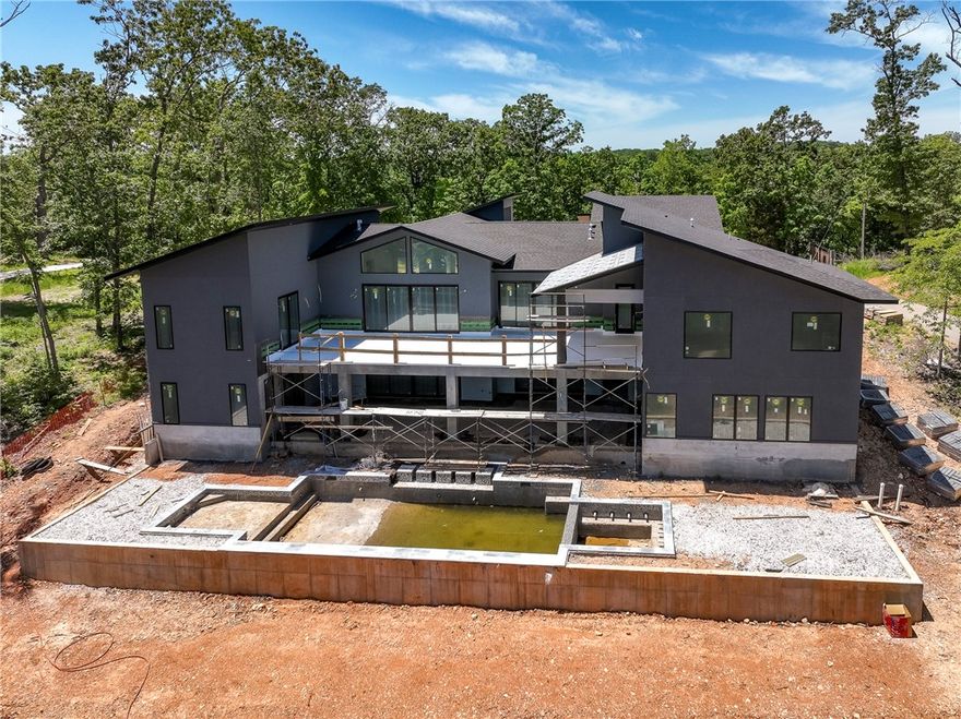 High above Beaver Lake in the gated community of Hawk’s Landing, this remarkable 7,000 sq. ft. waterfront estate blends modern luxury with breathtaking natural beauty. Enjoy sweeping lake views, a resort-style pool, and an oversized boat slip (2 for jet skis) at the new community dock. Architecturally striking with its sleek single-slope roof, stacked stone, and stucco exterior, the home offers a refined, contemporary presence. Inside, a wall of windows fills the space with natural light, highlighting a linear fireplace, custom white oak beams, and finely crafted cabinetry. The chef’s kitchen impresses with a 48” Thermador range, paneled appliances, and a seamless balance of style and function. The primary suite is a private retreat with a sloped ceiling, screened-in patio, and a spa-inspired European bath—all positioned to capture panoramic lake views. With over 2,000 sq. ft. of outdoor living space, expansive decks and patios, the home is ideal for entertaining or quiet relaxation. Request a full amenities sheet.