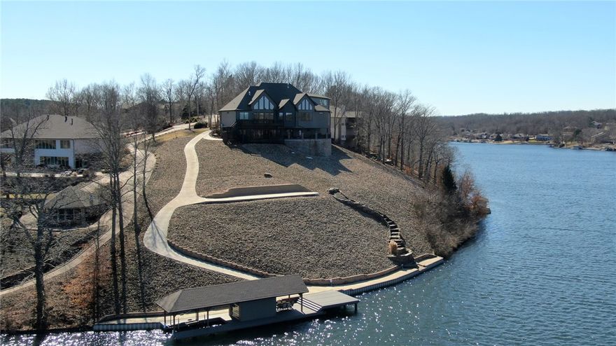 Lakefront estate on over an acre with panoramic views of beautiful Loch Lomond. Private boat house with a large dock for entertaining or enjoying the sun and all lake life has to offer. This immaculate home boasts an open floor plan perfect for entertaining with vaulted ceilings in the living room, an impressive floor-to-ceiling stone fireplace, an exquisite chef’s kitchen with a large island and eat-in area overlooking the lake. Wake up to gorgeous views of the lake from the primary suite. The spa-like bathroom features an oversized dual shower, generous soaking tub with views of the water, separate vanities, and an enormous walk-in closet.  You will love the lower living area complete with wine room and wet bar!  Enjoy boating, fishing, skiing on Bella Vista's largest lake!  Plus, you can take a short cruise to the marina and dine at Lakepoint Restaurant.