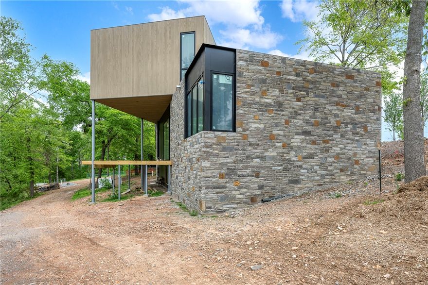 A refined expression of Ozark modernism, this architecturally significant residence in Nelagoney Glen draws inspiration from Frank Lloyd Wright, blending natural materials with intentional design. Rich walnut cabinetry anchors a sophisticated forest-inspired palette, creating warmth, depth, and understated luxury throughout. Clean lines, expansive glass, and seamless indoor-outdoor flow invite the surrounding landscape in, offering a sense of calm and privacy just minutes from downtown Bentonville. Designed by Modus Studio, every detail reflects craftsmanship and purpose—from curated finishes to the harmonious connection with nature. A rare opportunity to own a home where architecture, setting, and lifestyle converge at the highest level. This home will be ready in July. Renderings are conceptual and may vary from final construction. Images shown are from the model residence and are intended to represent the level of design, craftsmanship, and finishes to be delivered in this luxury home.