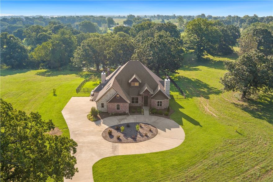 Seller offering $10K towards closing costs/ interest rate buy down with acceptable offer. This spectacular home sits on nine parklike acres with a pond. The home itself is a brick and stone stunner with upscale-rustic styling. Inside, lovely hardwood flooring flows through to rooms with features like shiplap, brick accent walls, coffered ceilings, abundant built-ins, and even a master closet tornado shelter.  The generous layout offers 5 beds and 4 full baths with energy-conscious extras like hybrid foam + insulation, 27 seer geothermal heating/cooling, trash compactor, and 3 woodburning fireplaces with gas starters. Creature comforts include primary bath with walk-in shower with rain showerheads, instant hot water, surround-sound and a new patio grill. Conveniences abound with double dishwashers and double ovens, two sets of w/d hookups, and a laundry room shower. And you'll never tire of delighting guests with the slide hidden behind an upstairs bookcase, whizzing both humans and clothing down to the laundry!