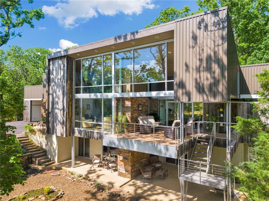 Architect-designed and offered for the first time, this exceptional East Fayetteville retreat sits on 7.7 private, wooded acres—an inspiring blend of modern design and natural beauty. Encompassing just under 3,600 SF, plus ~2,000 SF of covered outdoor living, the home seamlessly connects indoor and outdoor spaces with expansive glass and elevated views. Distinctive materials include Wyoming reclaimed snow fence, metal siding, and Arkansas native stone carried throughout the interior and exterior. The thoughtfully designed layout features 3 bedrooms, open living areas filled with natural light, and striking architectural details at every turn. Enjoy multiple covered patios, a serene forest setting, and a detached workshop for hobbies or storage. Tucked away in a peaceful, hidden setting yet just minutes from all Fayetteville amenities—this is a rare and remarkable offering.