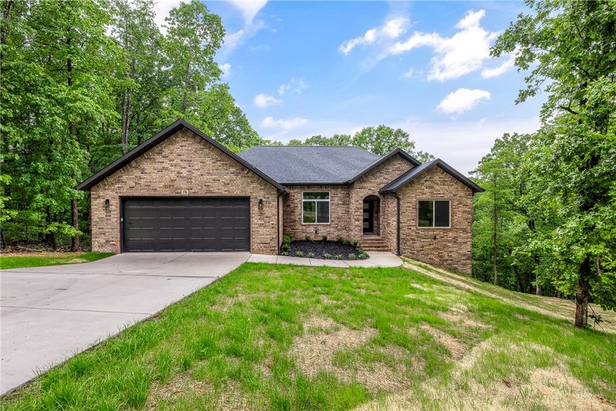 New construction on a beautiful double lot in the desirable southwest area of Bella Vista. Situated on approximately 0.59 acres, this property offers peaceful wooded views all around and is conveniently located near Lake Windsor, the Tunnel Vision bike trail, and Little Sugar Trails parking area. This thoughtfully designed single-level home features an open-concept layout with 11-foot ceilings in the main living area, a stacked-stone vent-free fireplace, and a walk-in pantry just off the kitchen. The large L-shaped kitchen opens into the main living and dining areas, creating an ideal space for entertaining. The split floor plan includes 3 bedrooms, 2 bathrooms, an office, and an oversized 2-car garage. The private primary suite features a walk-in closet along with a spacious bathroom offering dual vanities, a large tiled shower with dual shower heads, a linen closet, and a separate toilet room. Bedrooms 2 and 3 and the office are located on the opposite side of the home with a well-appointed hall bath nearby.